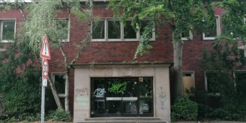 Ehemaliges Hallenbad Eickel in Herne aus rotem Klinker mit starkem Sanierungsbedarf in einer deutschen Innenstadt. Der Eingangsbereich ist von Graffiti verunstaltet, Bäume wachsen direkt an der Fassade. Das Gebäude wirkt verlassen und ungepflegt. Straßenschild mit Tempo-30-Zone im Vordergrund.