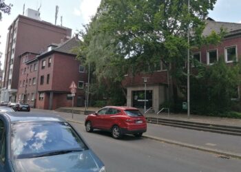 Hallenbad Eickel: Warum die Sanierung rechtlich, finanziell und politisch der einzig gangbare Weg ist Ehemaliges Hallenbad Eickel aus rotem Klinker in innerstädtischer Lage, mit graffitibeschmierter Eingangstür, umgeben von parkenden Autos, Bäumen und Gehweg – Straßenszene mit Tempo-30-Schild im Vordergrund.