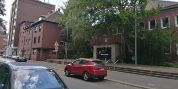 Ehemaliges Hallenbad Eickel aus rotem Klinker in innerstädtischer Lage, mit graffitibeschmierter Eingangstür, umgeben von parkenden Autos, Bäumen und Gehweg – Straßenszene mit Tempo-30-Schild im Vordergrund.