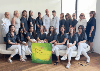 Das Team des Herner Hausarzt‑Praxis‑Zentrums zum 25-jährigen Jubiläum – Gruppenfoto mit Ärzten und medizinischen Fachangestellten vor neutralem Hintergrund, mit Logo-Tafel der Herner Hausärzte im Vordergrund.