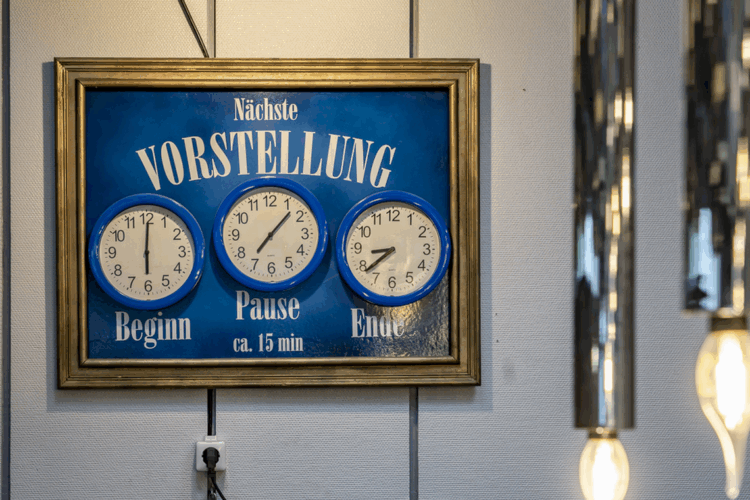 Uhrzeitentafel im Foyer des Mondpalasts Wanne-Eickel: Die analogen Uhren zeigen den Beginn, die Pause (ca. 15 Minuten) und das Ende der nächsten Vorstellung. Die nostalgische Anzeigetafel mit goldfarbenem Rahmen vermittelt Theateratmosphäre pur und gehört zu den beliebten Fotomotiven im Eingangsbereich des Volkstheaters.