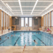 Modernisiertes Hallenbad Eickel mit vielen Schwimmer:innen im Becken, Holzverkleidung an den Wänden und original erhaltenen Wandmosaiken.