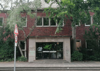 EFRE-Förderung für Hallenbad Eickel: Stadt Herne riskiert 8 Mio € Ehemaliges Hallenbad Eickel in Herne aus rotem Klinker mit starkem Sanierungsbedarf in einer deutschen Innenstadt. Der Eingangsbereich ist von Graffiti verunstaltet, Bäume wachsen direkt an der Fassade. Das Gebäude wirkt verlassen und ungepflegt. Straßenschild mit Tempo-30-Zone im Vordergrund.