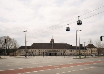 Seilbahn Herne: Der teuerste Blödsinn, den eine Stadt, die sich seit mehr als vier Jahrzehnten in der Haushaltssicherung befindet, erdenken kann Hauptbahnhof Wanne-Eickel (Herne) mit zwei Kabinen der urbanen Seilbahn, die über das Bahnhofsgebäude und den leeren Vorplatz schweben. Visualisierung des umstrittenen ÖPNV-Projekts General Blumenthal XI.