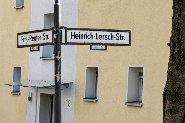 Heinrich Lersch Straße Herne: Graf Hotte hat Antrag auf Umbenennung eingereicht Straßenkreuzung Fritz-Reuter-Straße/Heinrich-Lersch-Straße in Herne Wanne-Eickel; Straßenschilder vor gelb-weißem Wohngebäude Nr. 18 und Baumstamm.