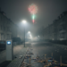 Nächtliche deutsche Wohnstraße im dichten Silvester-Smog mit einer Luftmessstation, Feuerwerksabfällen am Boden und einer Rakete am Himmel.