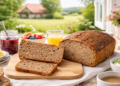 Modernes Frühstück im Landhaus: frisch geschnittenes Stefan´s Anti-Krebs-Brot (Vollkornbrot) auf Holzbrett, reich gedeckter Tisch und Blick ins Grüne durch das Fenster.