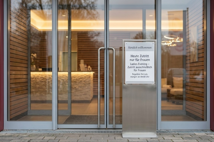 Ladies Abend im LAGO: „Ladies only“ als Wellness-Event oder als juristische Sollbruchstelle? Eingangsbereich eines modernen Spa-Resorts mit Hinweisschild zum exklusiven Ladies Evening. Heute Zutritt ausschließlich für Frauen. Genießen Sie Entspannung pur.