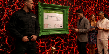 Sicherheitsbereich in einem Club mit Warteschlange, Security-Mitarbeiter und einem grün gerahmten Flucht- und Rettungsplan an einer rot beleuchteten Wand.