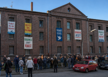 Manipulationsvorwurf am Hallenbad Eickel: Herner Stadtrat Ulrich behält sich strafrechtliche Prüfung vor Mahnwache vor ehemaligem Gefängnisgebäude in Eickel mit bunten Bannern an vergitterten Fenstern für Hallenbad, Freiheit und Bürgerwillen.