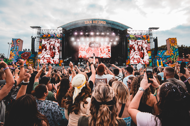 Besucher:innen vor der farbenfrohen Mainstage des San Hejmo Festivals am Airport Weeze während eines Liveauftritts.