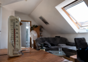 Hitze im Dachgeschoss: Wann fehlende Dämmung zum Mangel wird Innenansicht einer aufgeheizten Dachgeschosswohnung mit Dachschrägen, Thermometer ohne lesbare Werte und starkem Sonnenlichteinfall.