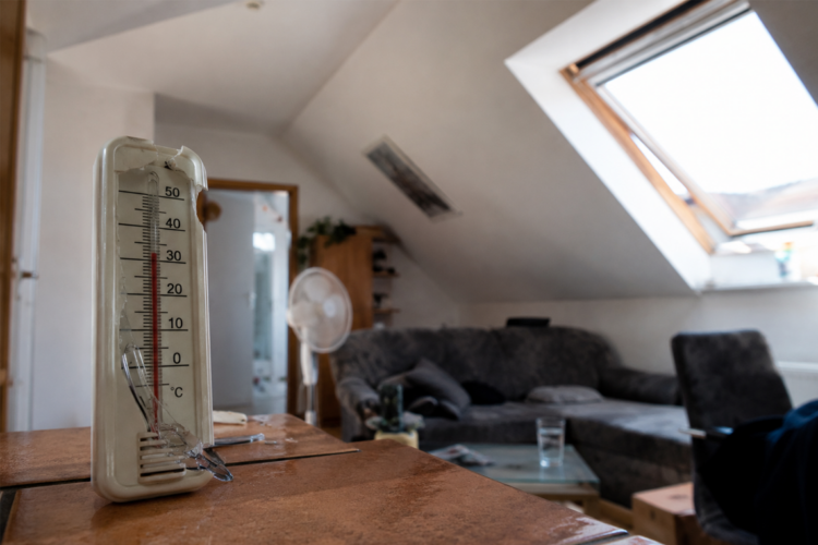 Hitze im Dachgeschoss: Wann fehlende Dämmung zum Mangel wird Innenansicht einer aufgeheizten Dachgeschosswohnung mit Dachschrägen, Thermometer ohne lesbare Werte und starkem Sonnenlichteinfall.