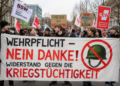 Wehrpflicht – Nein danke: Widerstand gegen die neue Kriegstüchtigkeit Junge Demonstrant:innen protestieren mit einem großen Banner gegen Wehrpflicht und Kriegstüchtigkeit; im Hintergrund sind weitere Teilnehmende mit Friedens- und Gewerkschaftsschildern zu sehen.