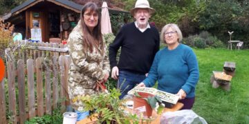 Drei gut gelaunte Personen im herbstlichen Garten an einem Tisch mit Topfpflanzen, Wurzelballen und einem Pflanzenbuch während der 59. Herner Pflanzentauschbörse.
