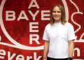 Michelle Böhmke leitet künftig Bayer 04s Haus der Talente Michelle Böhmke übernimmt im Sommer 2027 die Leitung des Hauses der Talente von Bayer 04 Leverkusen und steht vor einer roten Vereinswand.