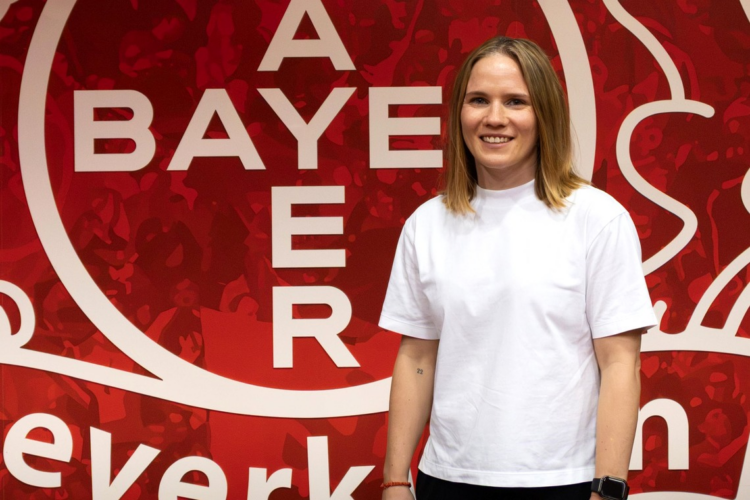 Michelle Böhmke leitet künftig Bayer 04s Haus der Talente Michelle Böhmke übernimmt im Sommer 2027 die Leitung des Hauses der Talente von Bayer 04 Leverkusen und steht vor einer roten Vereinswand.