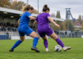 SGS Essen empfängt den VfL Bochum zum Revierduell Zwei Fußballerinnen in blauen und violetten Trikots kämpfen auf einem Fußballplatz um den Ball.