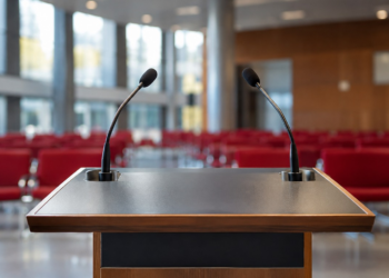 Juso-Chef Türmer fordert Kurswechsel in SPD und Koalition Leeres Rednerpult mit zwei Mikrofonen vor den roten Sitzreihen eines Veranstaltungssaals.