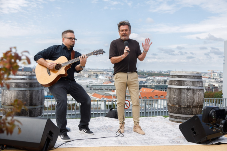 Thomas Anders berichtet von 30 Millionen neuen Streams Thomas Anders mit Mikrofon und ein Gitarrist auf einer Dachterrasse.