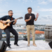 Thomas Anders mit Mikrofon und ein Gitarrist auf einer Dachterrasse.