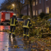 Sturmböen in Herne: Feuerwehr bei zahlreichen Einsätzen Zwei Feuerwehrkräfte neben herabgefallenen Ästen auf einer nassen Wohnstraße mit einem roten Einsatzfahrzeug.